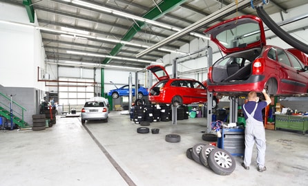 Reifenwechsel und Reparatur von Autos in einer Werkstatt - Aussstattung und Mechaniker arbeitet am Fahrzeug auf einer Hebebühne